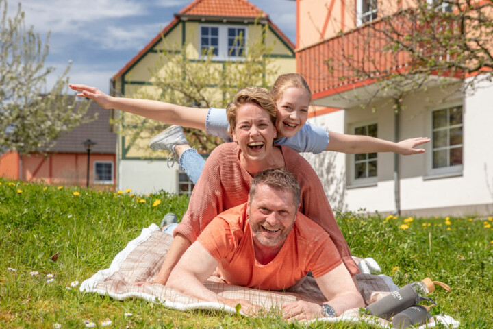 Mutter, Vater, Tochter liegen auf einer Picknickdecke im Familienresort am Fleesensee