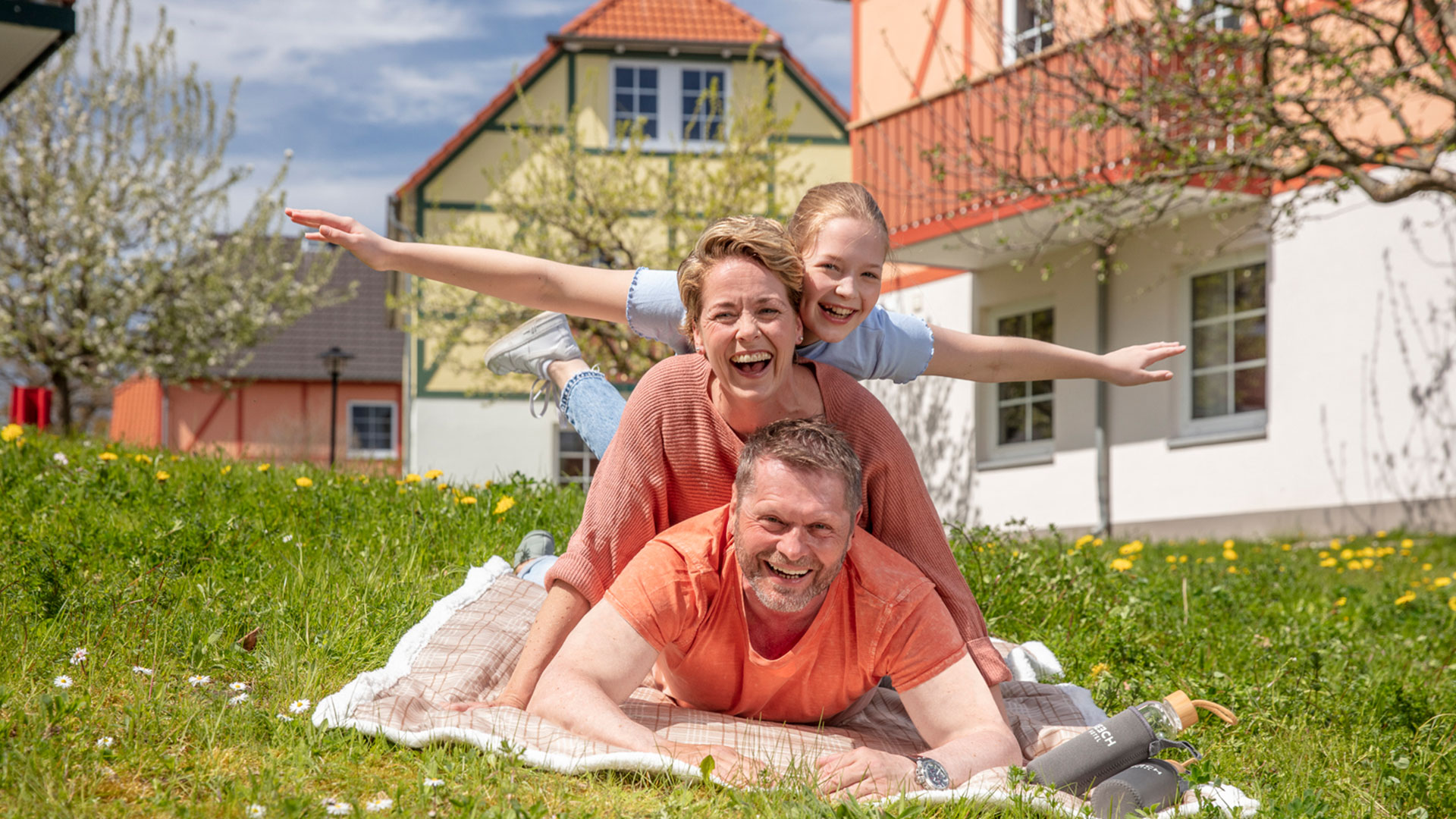 Mutter, Vater, Tochter liegen auf einer Picknickdecke im Familienresort am Fleesensee