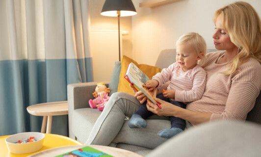Familienzeit im Appartement vom BEECH Resort Fleesensee | Mama schaut mit Kleinkind ein Buch an