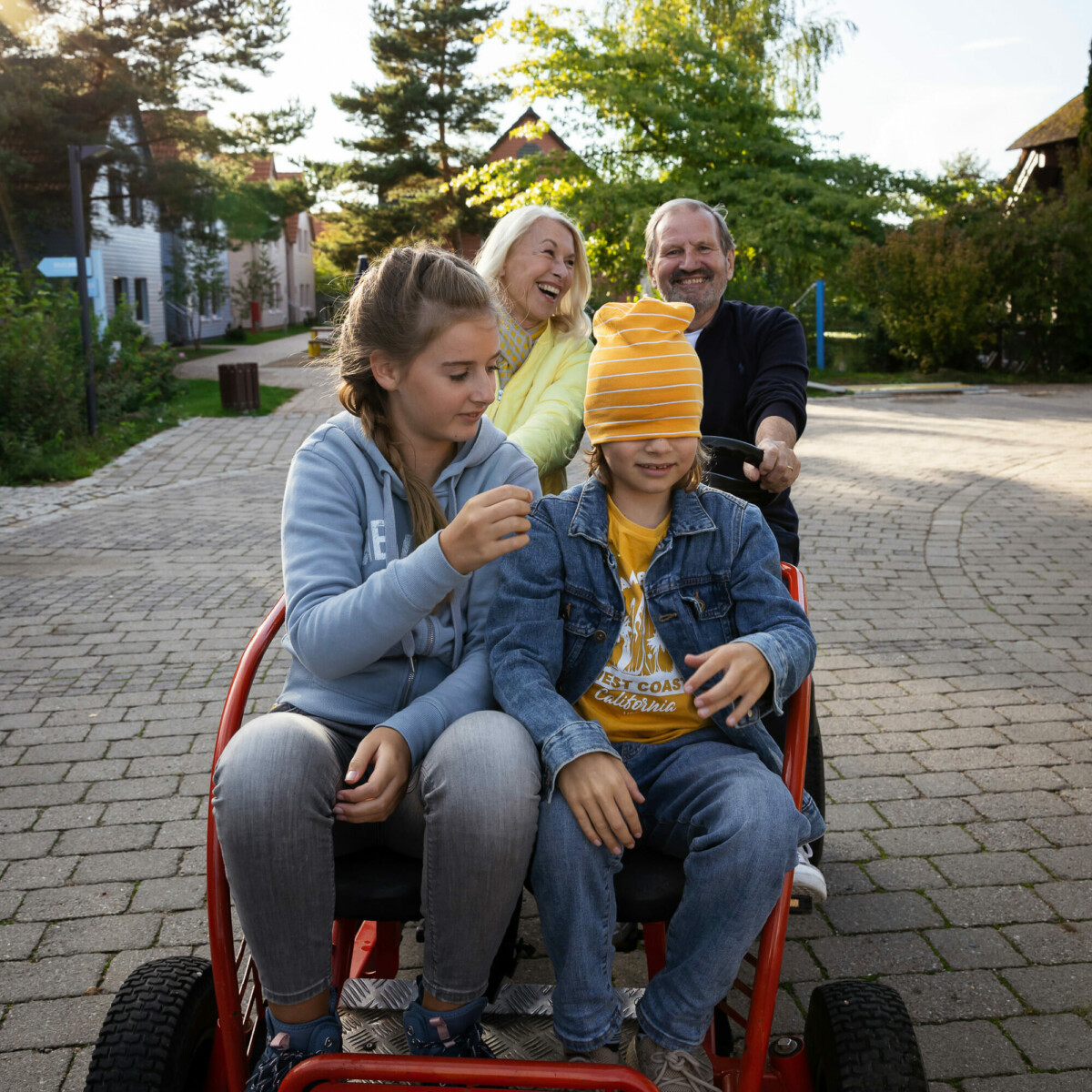 Oma, Opa im Urlaub mit Enkelkinder auf dem Kettcar unterwegs durch das Familienresort