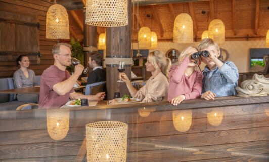 Familie sitzt im Restaurant am Fleesensee und Kinder gucken durch ein Fernglas zum Familienresort