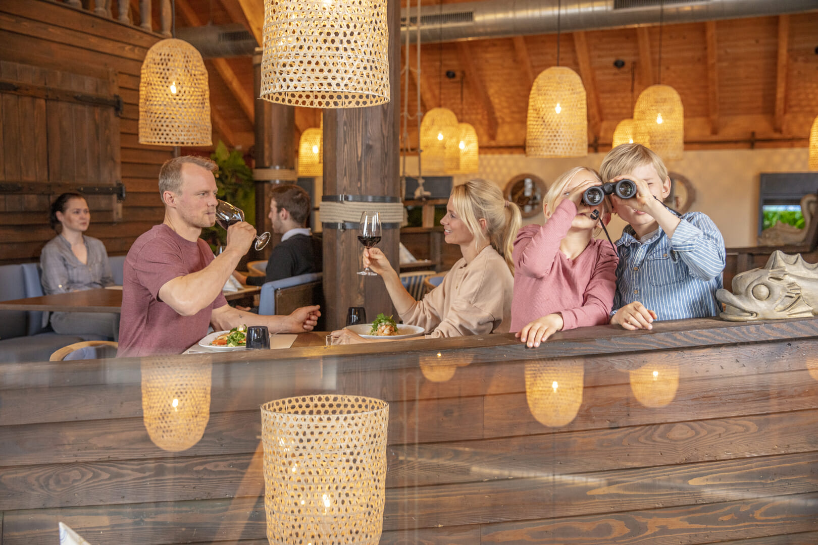 Familie sitzt im Restaurant am Fleesensee und Kinder gucken durch ein Fernglas zum Familienresort